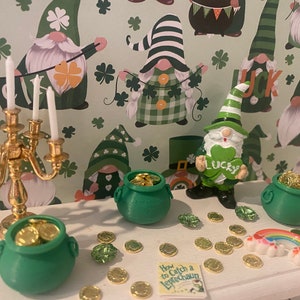 Puede incluir: Una mesa blanca con un candelero dorado, tres ollas de oro verdes, un arco&iacute;ris y un libro titulado "C&oacute;mo atrapar un duende". La mesa est&aacute; decorada con monedas de oro y tr&eacute;boles verdes. El fondo es un patr&oacute;n verde y blanco con gnomos que llevan sombreros verdes.