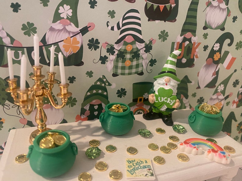 Puede incluir: Una mesa blanca con un candelero dorado, tres ollas de oro verdes, un arco&iacute;ris y un libro titulado "C&oacute;mo atrapar un duende". La mesa est&aacute; decorada con monedas de oro y tr&eacute;boles verdes. El fondo es un patr&oacute;n verde y blanco con gnomos que llevan sombreros verdes.
