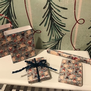 Puede incluir: Un conjunto de suministros para envolver regalos de Navidad con un patr&oacute;n azul y blanco con Pap&aacute; Noel y otros personajes navide&ntilde;os. El conjunto incluye dos bolsas de regalo, un rollo de papel de regalo y una peque&ntilde;a caja de regalo con una cinta azul.