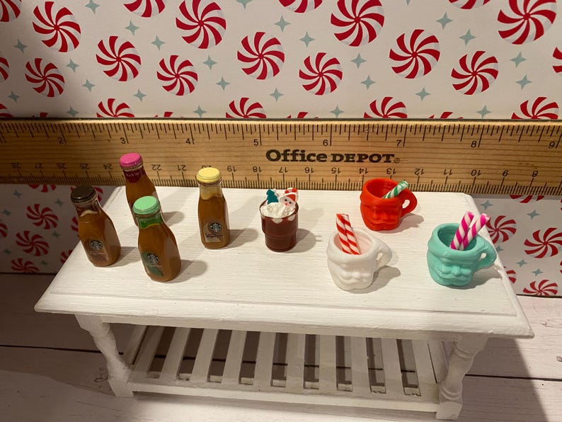Pode incluir: Uma mesa branca com uma variedade de garrafas e canecas em miniatura. As garrafas s&atilde;o de vidro transparente com l&iacute;quido castanho no interior e tampas coloridas. As canecas s&atilde;o brancas, vermelhas e azuis com agitadores de pau de cana-de-a&ccedil;&uacute;car. A mesa tem uma superf&iacute;cie branca e pernas brancas.