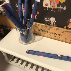 Puede incluir: Un tarro de vidrio lleno de tubos de papel de Halloween azules y blancos. Los tubos est&aacute;n decorados con murci&eacute;lagos, fantasmas y calabazas. El tarro est&aacute; sentado en una mesa blanca con una regla de madera que dice "Office Depot".