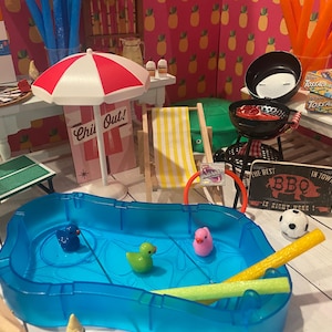 Puede incluir: Una escena de verano en miniatura con una piscina azul, patos y un fideo de piscina amarillo. Otros elementos incluyen una sombrilla a rayas rojas y blancas, una parrilla, una mesa de ping pong y un letrero que dice "The Best BBQ In Town".