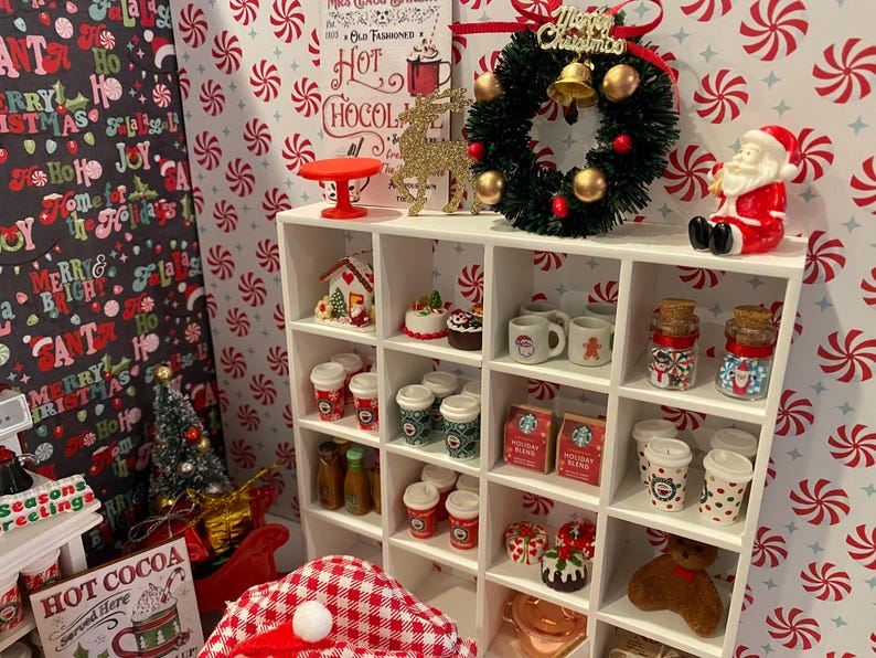 Pode incluir: Uma estante branca com uma variedade de itens tem&aacute;ticos de Natal, incluindo uma coroa, uma casa de gengibre, canecas e jarros. A estante &eacute; decorada com um padr&atilde;o de bengalas de doces vermelhas e brancas.