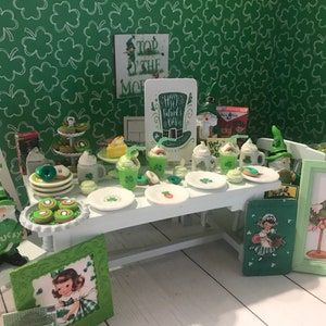 Puede incluir: Una escena en miniatura con temática del Día de San Patricio con una mesa blanca llena de golosinas, bebidas y decoraciones. La escena incluye platos, tazas, postres y obras de arte enmarcadas, todo en tonos verdes y blancos. También hay una figura de gnomo y un letrero que dice "Happy Patrick's Day".