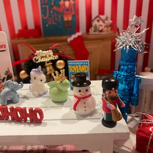 May include: A festive Christmas display featuring miniature figurines, including a giraffe, elephant, unicorn, snowman, and soldier. The word "HOHOHO" is displayed in red. A blue Christmas tree and a red gift box are also present.