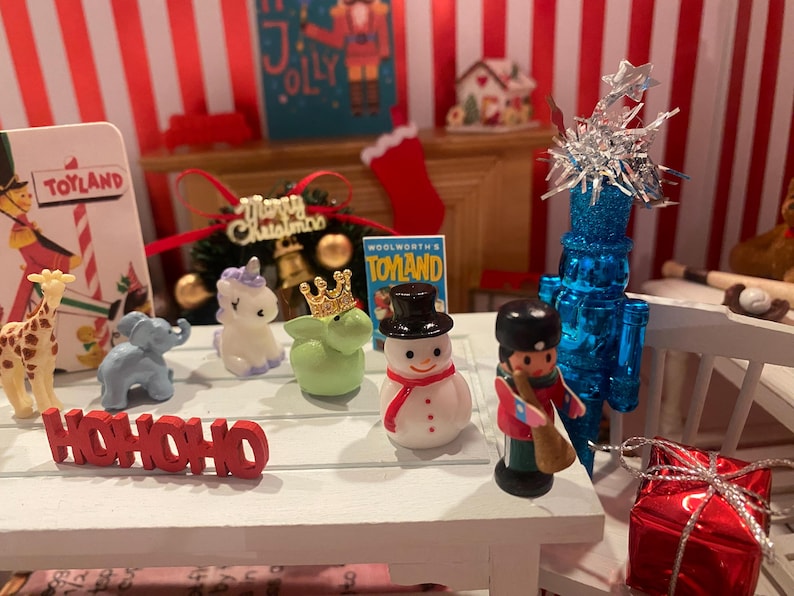 May include: A festive Christmas display featuring miniature figurines, including a giraffe, elephant, unicorn, snowman, and soldier. The word "HOHOHO" is displayed in red. A blue Christmas tree and a red gift box are also present.
