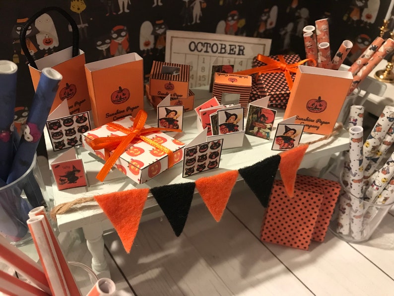 Puede incluir: Un escaparate en miniatura con tem&aacute;tica de Halloween con decoraciones naranjas y negras. La tienda ofrece una variedad de art&iacute;culos, incluyendo cajas de regalo, papel de regalo y tarjetas. La tienda est&aacute; decorada con una pancarta que dice "OCTUBRE" y un calendario con el mes de octubre resaltado.