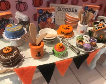 Könnte beinhalten: Ein Miniatur-Küchenset zum Thema Halloween mit einer Auswahl an Kuchen, Cupcakes und anderen Leckereien. Das Set enthält einen kleinen Mixer, einen Holz-Löffelhalter, einen Schneebesen und einen Kalender mit dem Wort "OKTOBER" darauf.