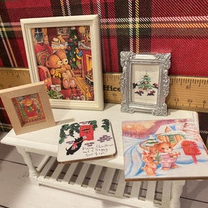 Puede incluir: Una colecci&oacute;n de arte y decoraci&oacute;n navide&ntilde;a en miniatura. Incluye cuadros enmarcados con osos de peluche y un &aacute;rbol de Navidad, y un posavasos con un perro y un buz&oacute;n. Los art&iacute;culos est&aacute;n dispuestos sobre una peque&ntilde;a mesa blanca.