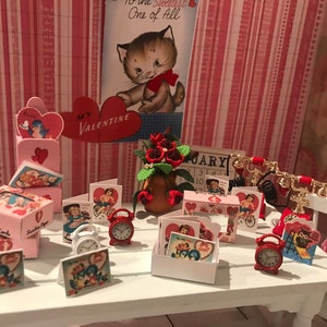 May include: A miniature Valentine's Day scene with a pink and white table, red alarm clocks, a red phone, and a variety of Valentine's Day cards and boxes. The background is a pink and white striped wallpaper with hearts.