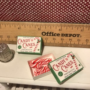 May include: Miniature Christmas candy canes and boxes with the text "Candy Canes" and "North Pole's Finest". The boxes are green and white, and the candy canes are red and white striped.