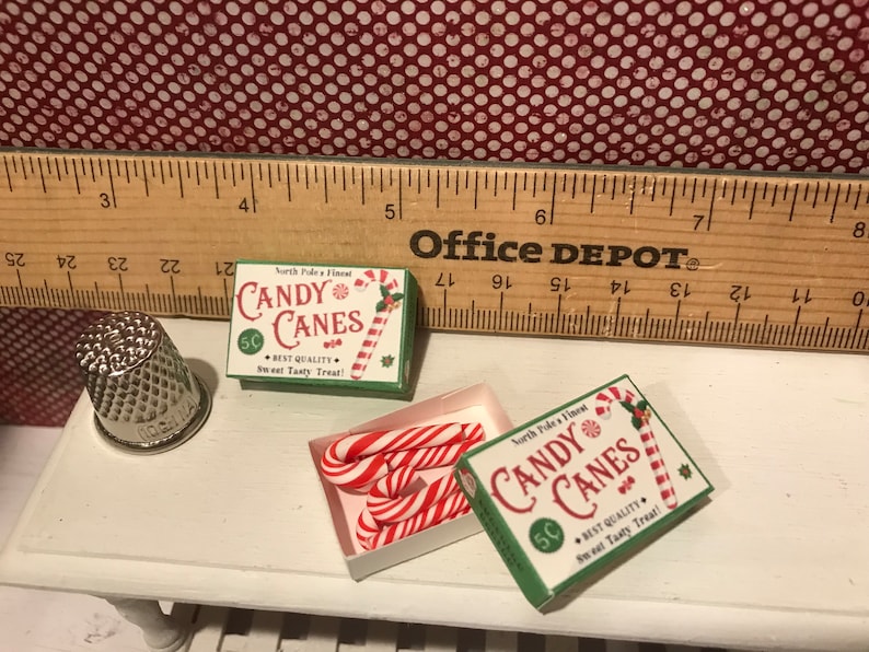May include: Miniature Christmas candy canes and boxes with the text "Candy Canes" and "North Pole's Finest". The boxes are green and white, and the candy canes are red and white striped.