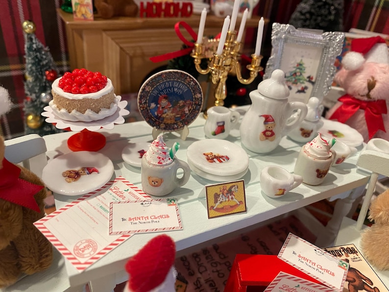 Puede incluir: Una escena navide&ntilde;a en miniatura con una mesa blanca decorada con art&iacute;culos festivos. Incluye un pastel, platos, una tetera, tazas y un marco de fotos. Los art&iacute;culos est&aacute;n decorados con osos de peluche y motivos navide&ntilde;os.