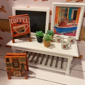 Pode incluir: Uma pequena mesa branca exibe uma imagem emoldurada de um tigre em uma banheira, um quadro-negro e letreiros de caf&eacute;. Pequenas suculentas em vasos e pequenas x&iacute;caras de caf&eacute; tamb&eacute;m est&atilde;o sobre a mesa. O fundo apresenta papel de parede com tema de tigre.