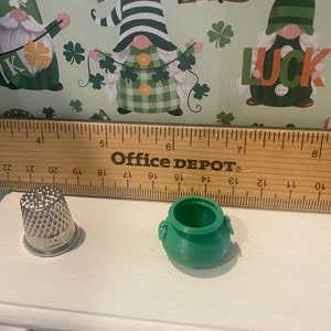 Puede incluir: Una olla verde con dos asas y un dedal de plata. La olla y el dedal est&aacute;n sobre una superficie blanca junto a una regla de madera con las palabras "Office Depot" impresas en ella.