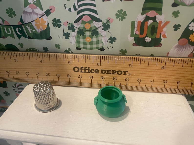 Puede incluir: Una olla verde con dos asas y un dedal de plata. La olla y el dedal est&aacute;n sobre una superficie blanca junto a una regla de madera con las palabras "Office Depot" impresas en ella.