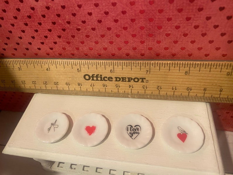 Puede incluir: Cuatro peque&ntilde;os platos de cer&aacute;mica blanca con diferentes dise&ntilde;os. Un plato tiene un unicornio, uno tiene un coraz&oacute;n, uno dice "Te amo" con un coraz&oacute;n y uno tiene un p&aacute;jaro con un coraz&oacute;n.