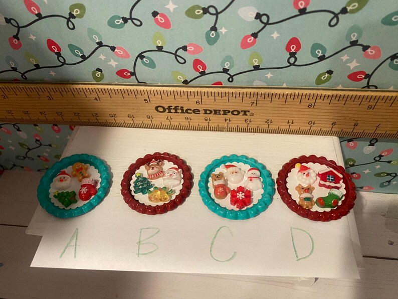 May include: Four Christmas-themed bottle caps with red and blue trim. Each cap features a different holiday scene with Santa Claus, reindeer, and other festive elements. The caps are labeled A, B, C, and D.
