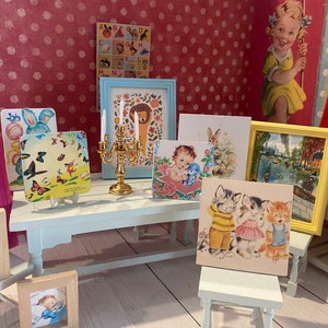 Puede incluir: Una colecci&oacute;n de ilustraciones y obras de arte enmarcadas de estilo vintage, que incluyen im&aacute;genes de un le&oacute;n, gatitos, un beb&eacute; y mariposas. Tambi&eacute;n hay un candelabro dorado y una peque&ntilde;a mesa blanca. El fondo presenta una pared rosa con lunares.