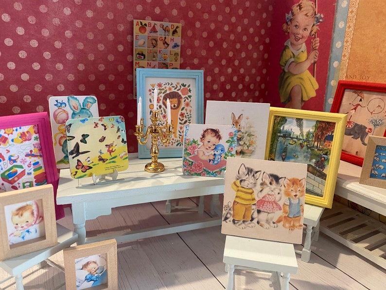 Puede incluir: Una colecci&oacute;n de ilustraciones y obras de arte enmarcadas de estilo vintage, que incluyen im&aacute;genes de un le&oacute;n, gatitos, un beb&eacute; y mariposas. Tambi&eacute;n hay un candelabro dorado y una peque&ntilde;a mesa blanca. El fondo presenta una pared rosa con lunares.