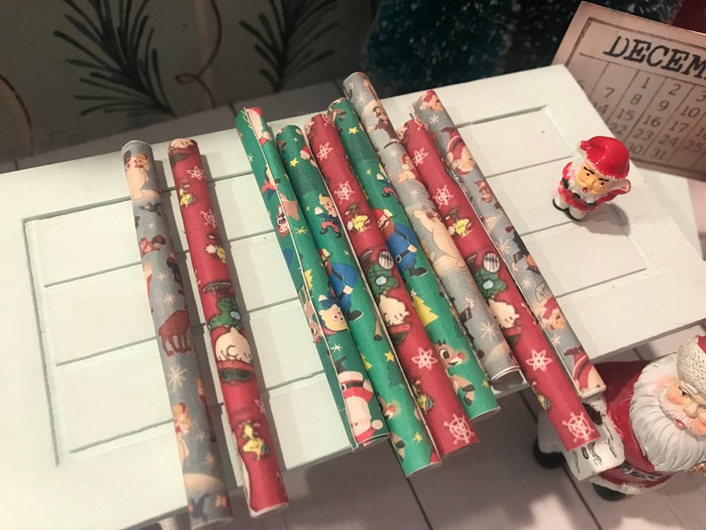 Puede incluir: Surtido de ocho rollos de papel de regalo de Navidad con varios dise&ntilde;os de tem&aacute;tica navide&ntilde;a que incluyen Pap&aacute; Noel, renos y copos de nieve. El papel es rojo, verde y azul con detalles blancos.