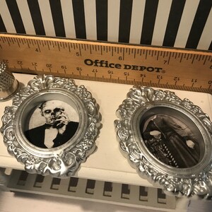May include: Two silver-colored, ornate oval frames with black and white images of classic horror characters. A silver thimble and a wooden ruler are also in the image. The ruler has the text "Office DEPOT" printed on it.