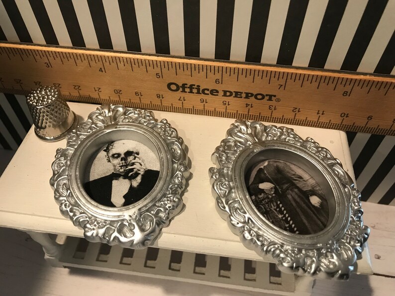 May include: Two silver-colored, ornate oval frames with black and white images of classic horror characters. A silver thimble and a wooden ruler are also in the image. The ruler has the text "Office DEPOT" printed on it.