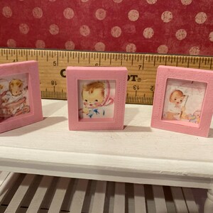 Puede incluir: Tres peque&ntilde;as im&aacute;genes enmarcadas en rosa con ilustraciones de beb&eacute;s vintage. Los marcos son cuadrados y est&aacute;n sobre una mesa blanca. Una regla de madera est&aacute; en el fondo. Las im&aacute;genes de beb&eacute;s son en colores pastel suaves.