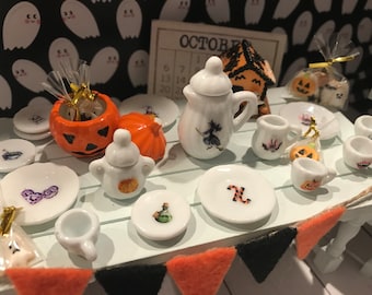 Könnte beinhalten: Ein Miniatur-Teeservice aus weißer Keramik mit Halloween-Motiven wie einer Hexe, Kürbissen, Geistern und Zaubertränken. Das Set besteht aus kleinen Tellern, Tassen, einer Teekanne und einer Zuckerdose mit Deckel sowie kleinen Geschenktüten.