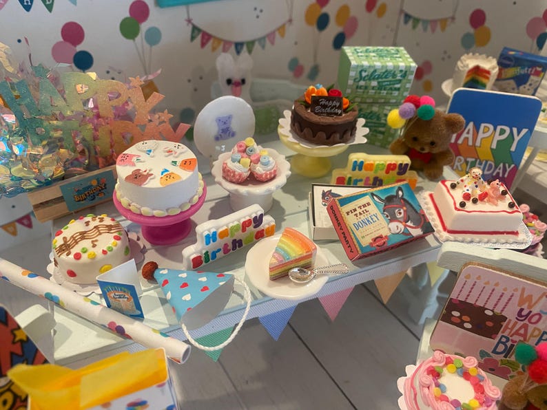 May include: A collection of miniature birthday-themed items, including cakes, party hats, and a teddy bear. The scene includes a cake with the words "Happy Birthday" and a vintage "Pin the Tail on the Donkey" game.