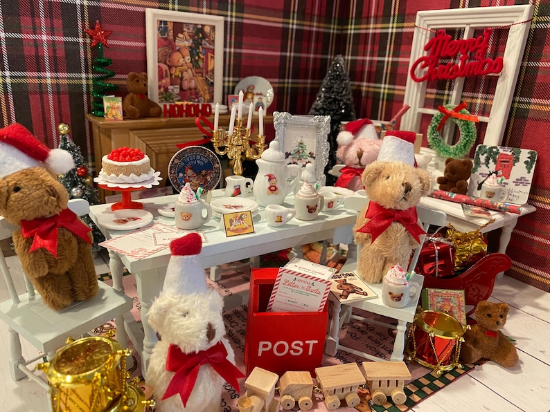Puede incluir: Una escena navide&ntilde;a festiva con osos de peluche en miniatura, un pastel y un &aacute;rbol de Navidad en miniatura. La escena incluye un buz&oacute;n rojo, un tambor en miniatura y un letrero que dice "Merry Christmas".
