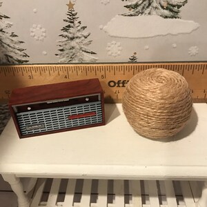 May include: A miniature wooden radio with a red and silver design sits on a white table next to a ball of twine.