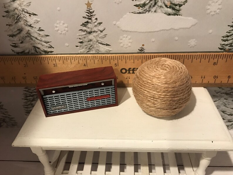 May include: A miniature wooden radio with a red and silver design sits on a white table next to a ball of twine.