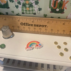 Puede incluir: Una mesa en miniatura blanca con un arco&iacute;ris, un tr&eacute;bol y monedas de oro. La mesa tiene un estante debajo. Una regla con el texto "Office Depot" est&aacute; encima de la mesa.