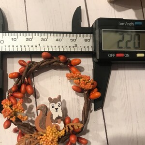 May include: A brown twig wreath with orange berry accents and a small wooden squirrel figurine. The wreath measures 220 mm in diameter.