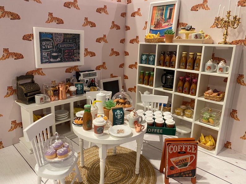Pode incluir: Cena de caf&eacute; em miniatura com uma mesa branca, cadeiras e prateleiras cheias de x&iacute;caras de caf&eacute;, garrafas e doces. Uma placa diz "Coffee Fresh Brewed Best in Town". As paredes s&atilde;o decoradas com uma estampa de tigre.