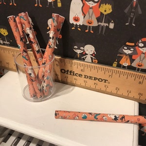 Puede incluir: Un tarro de vidrio lleno de l&aacute;pices de color naranja y blanco con tem&aacute;tica de Halloween. Los l&aacute;pices tienen un patr&oacute;n en blanco y negro de gatos, fantasmas y calabazas. El tarro est&aacute; sentado en una mesa blanca junto a una regla de madera con la etiqueta "Office Depot".