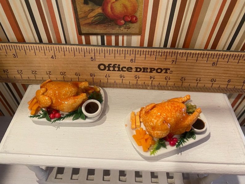 May include: Two miniature roasted chicken dishes on white plates. Each plate includes a golden-brown chicken, french fries, vegetables, and a small bowl of gravy. The dishes are set on a white surface.