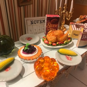May include: Miniature Thanksgiving table setting with a roasted turkey, corn on the cob, a pumpkin, and a blueberry tart. Includes miniature boxes of Stove Top and Hungry Jack. A small calendar shows the month of November.