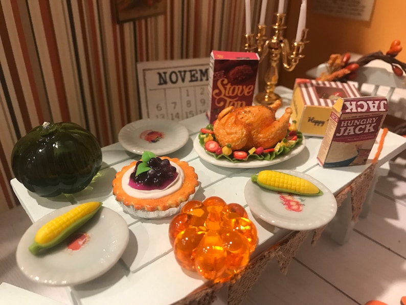 May include: Miniature Thanksgiving table setting with a roasted turkey, corn on the cob, a pumpkin, and a blueberry tart. Includes miniature boxes of Stove Top and Hungry Jack. A small calendar shows the month of November.