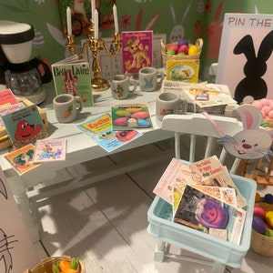 May include: A miniature Easter-themed scene with a white table, books, mugs, and a coffee maker. The table is set with books, magazines, and mugs with Easter-themed designs. A sign reads "Pin the Tail". A basket holds colorful Easter eggs.