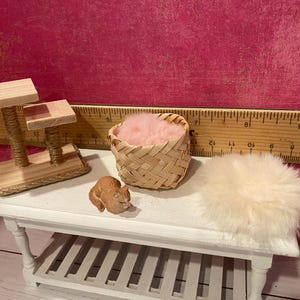 K&ouml;nnte beinhalten: Ein Miniatur-Kratzbaum aus Holz mit zwei Plattformen, ein kleiner geflochtener Korb mit rosa Kunstfell, eine winzige braune Katzenfigur und ein runder wei&szlig;er Kunstfellteppich. Ein Holzlineal im Hintergrund zeigt eine Skala von 30 Zentimetern.