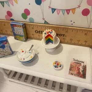 May include: Miniature scene featuring a rainbow cake slice on a pedestal, a bowl of whipped cream with sprinkles, and a box of confetti cake mix. A small bowl of colorful candies and a card that reads "I'm throwing a party" are also present.