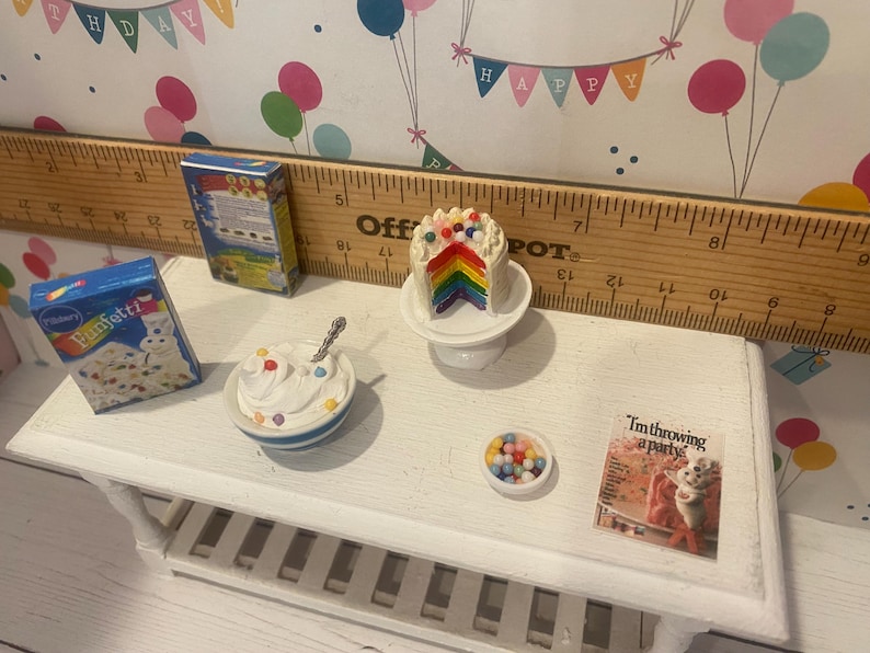 May include: Miniature scene featuring a rainbow cake slice on a pedestal, a bowl of whipped cream with sprinkles, and a box of confetti cake mix. A small bowl of colorful candies and a card that reads "I'm throwing a party" are also present.