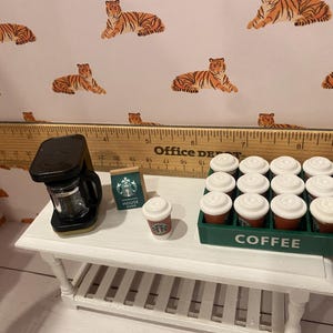Pode incluir: Cena de caf&eacute; em miniatura com uma cafeteira preta, um saco de caf&eacute; Starbucks e uma x&iacute;cara de caf&eacute; pequena. Uma bandeja verde cont&eacute;m uma d&uacute;zia de x&iacute;caras de caf&eacute; em miniatura. O fundo apresenta uma estampa de tigre.