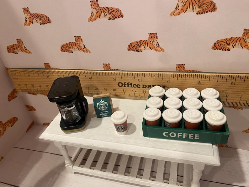Pode incluir: Cena de caf&eacute; em miniatura com uma cafeteira preta, um saco de caf&eacute; Starbucks e uma x&iacute;cara de caf&eacute; pequena. Uma bandeja verde cont&eacute;m uma d&uacute;zia de x&iacute;caras de caf&eacute; em miniatura. O fundo apresenta uma estampa de tigre.