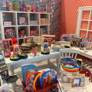Könnte beinhalten: Eine Miniatur-Spielzeugladenausstellung mit verschiedenen Spielzeugen und Spielen. Die Ausstellung umfasst Puppen, Brettspiele und ein Lite-Brite-Set. Das Farbschema ist hell und verspielt, mit einem roten Wagen voller bunter Ringe und einem roten Roller.