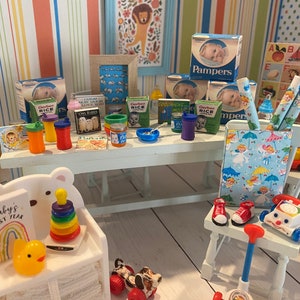 May include: A miniature dollhouse nursery with a white table, a white chair, and a white shelf. The table is set with miniature baby food jars, cereal boxes, and a blue bowl. The chair has a red and white phone and a red and white toy on it. The shelf has a rainbow toy, a yellow rubber duck, and a stacking ring toy.