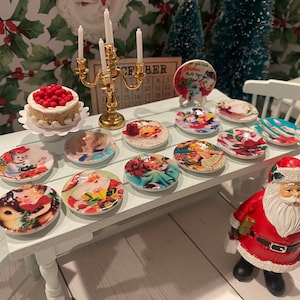 May include: A miniature Christmas table setting with a white cake, a gold candelabra, and a variety of small plates with festive designs. The plates feature images of Santa Claus, snowmen, and other Christmas imagery. A small Santa Claus figurine stands on the table.