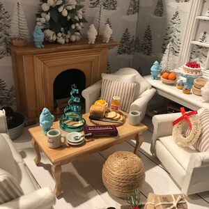 May include: A miniature living room scene with a white fireplace, two white armchairs with striped cushions, a coffee table with a game of Pictionary, a blue Christmas tree, and a blue snowman figurine.